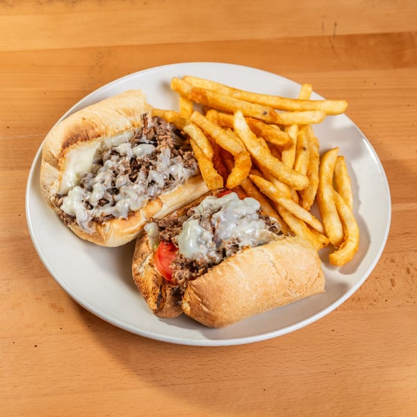 Two cheesesteak sandwiches with melted cheese and a side of golden french fries on a white plate.