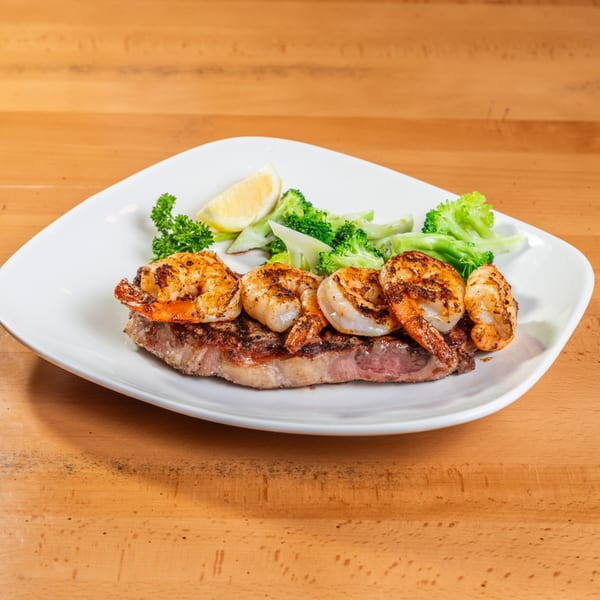 Rincon Italian Grill's steak and shrimp entree with broccoli and a lemon wedge on a white plate.