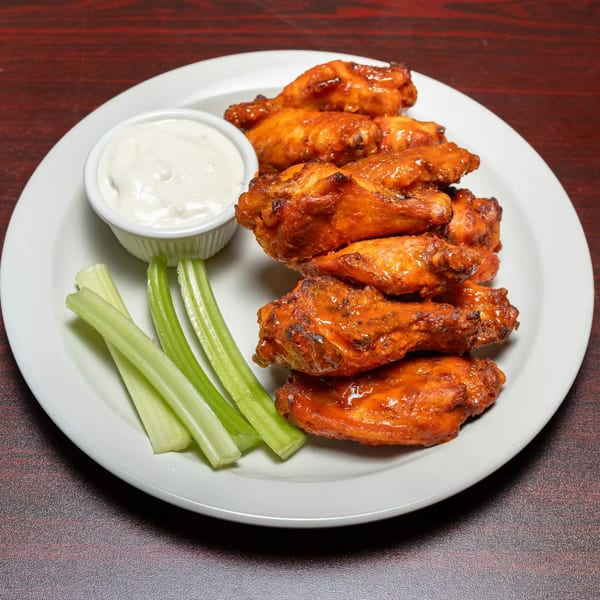 A plate of buffalo chicken wings with celery sticks and a side of ranch dressing.