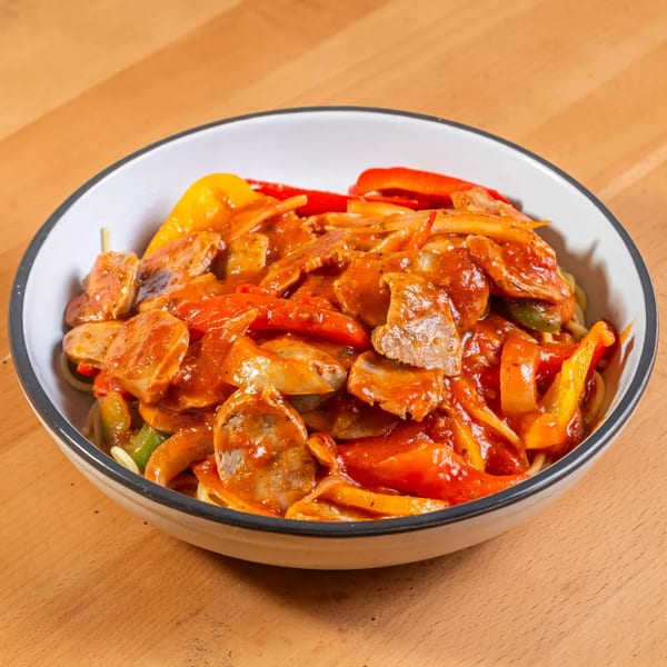A white bowl filled with Italian sausage, red and yellow bell peppers, and onions in a rich tomato sauce.