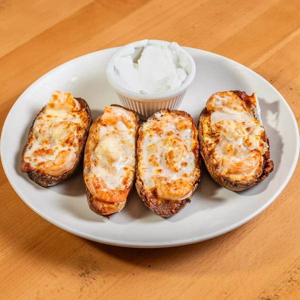 Four shrimp bruschetta with melted cheese and a side of white dipping sauce on a white plate.